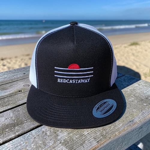 Redcastaway black trucker cap with white mesh back and embroidered sunset logo. Features a flat bill and snapback closure.