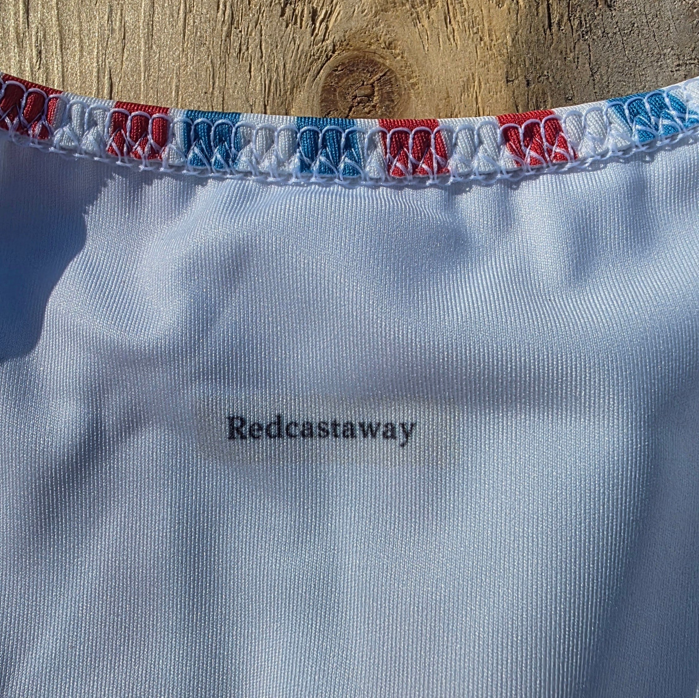 Redcastaway™ white one-piece swimsuit with a red and blue striped trim, scoop neckline, and cheeky fit.